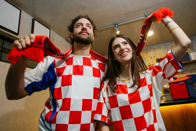Two football fans in checkered jerseys and a scarf cheering during a match.